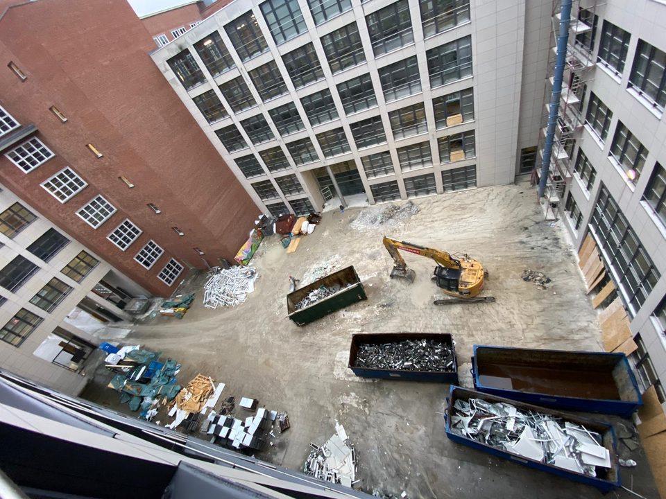 Baustellenübersicht im Innenhof mit Bagger und Containern voller Fensterrahmen
